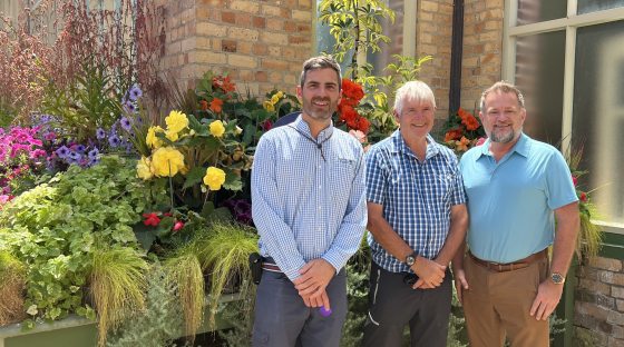 Three people standing in front of colorful flowers smiling.